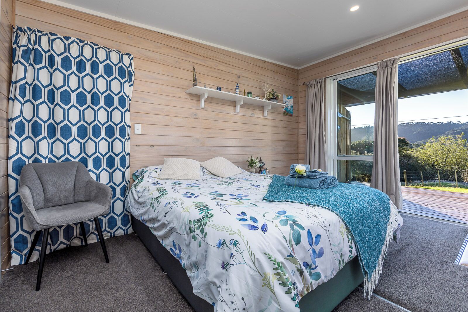 Ein Schlafzimmer mit einem Bett, einem Sessel, einem Fenster mit Blick und einem Regal mit Dekoration.