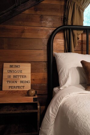 A wooden bed with white bedding and a pillow, a bedside table with a lamp, and a sign with an inspirational quote.
