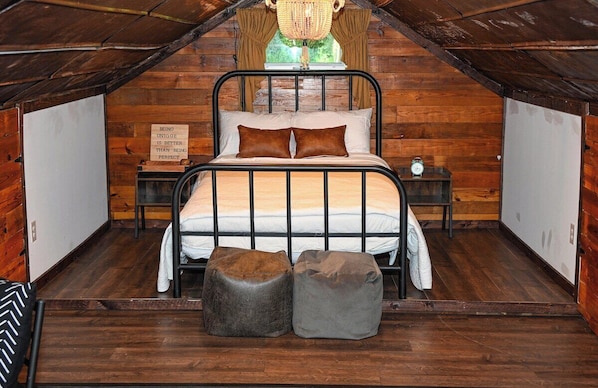 A cozy attic bedroom with a metal bed frame, two nightstands, a chandelier, and a wooden wall. - Baurenhaus - The Farmhouse (Marble)