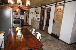 A kitchen with a wooden table, white chairs, a coffee machine, and a vintage-style washroom door.