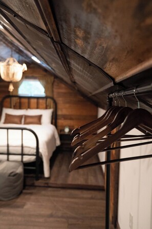 A bedroom with a bed, a hanging light fixture, and a coat rack.