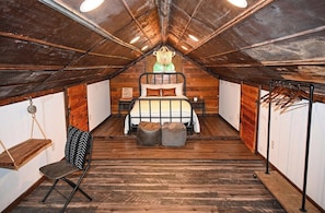 Una camera da letto in stile loft con soffitto a falde, un letto con copripiumino a righe bianche e gialle, una poltrona sospesa e una panca in legno.