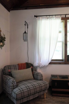 A plaid armchair with a cushion, a hanging light fixture, a window with curtains, and a wooden chest.