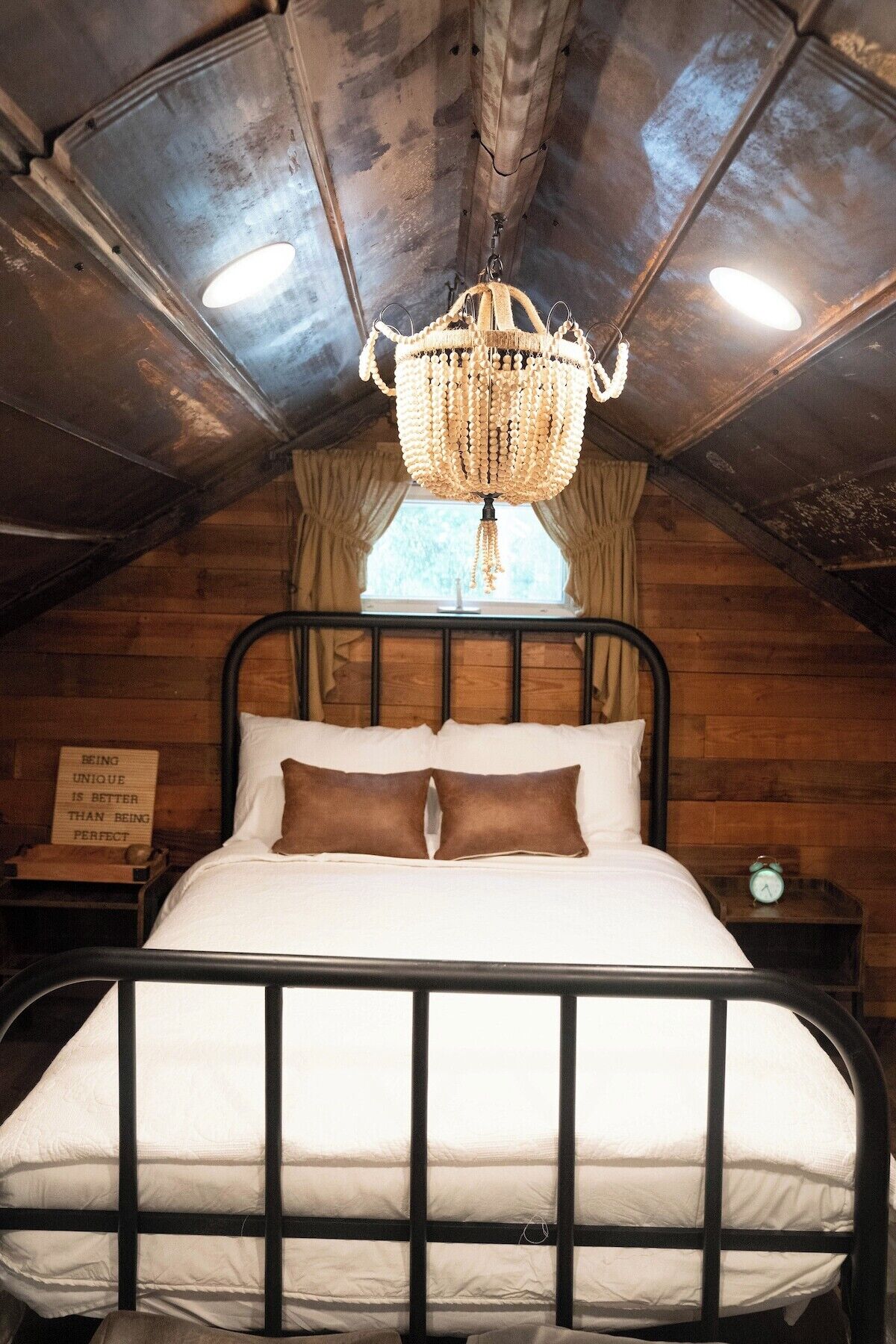 Une chambre confortable avec un lit en métal, un lustre orné de guirlandes de perles et une fenêtre avec des rideaux.