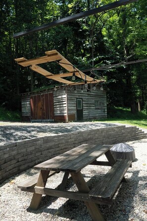 Un tavolo da picnic con panchina, circondato da un'area ghiaiosa, con una struttura in legno sopra e un piccolo edificio sullo sfondo.