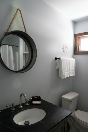 Un bagno con uno specchio rotondo, un lavandino con rubinetto, un water e un porta asciugamani.