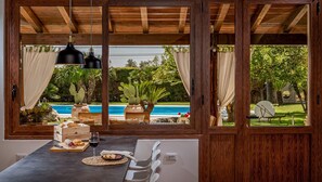 Comedor con vistas a una piscina y follaje, techo de madera y una mesa dispuesta con comida y bebidas.