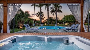 A hot tub with lounge chairs and a pool, surrounded by palm trees and a wooden deck. - Villa Cutrera 6 Emma Villas (Chiaramonte Gulfi)