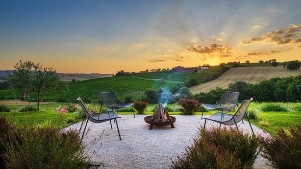 A patio with two chairs and a fire pit, overlooking a vineyard and rolling hills during sunset. - Villa Flaminia 8 2 - Emma Villas (Gualdo Cattaneo)