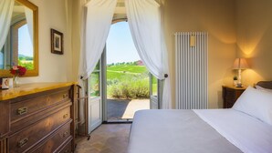 A bedroom with a bed, a dresser, a window with curtains, a radiator, and a view of a vineyard. - Villa Flaminia 8 2 - Emma Villas (Gualdo Cattaneo)