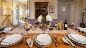 A dining table set for six with white plates, silverware, and wine glasses, a vase with white flowers, and a bottle of wine. - Villa Flaminia 8 2 - Emma Villas (Gualdo Cattaneo)