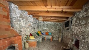 A rustic stone-walled room with a brick fireplace, wooden ceiling beams, and a bench with colorful cushions. - La Posada de Don Luis (Ezequiel Montes)