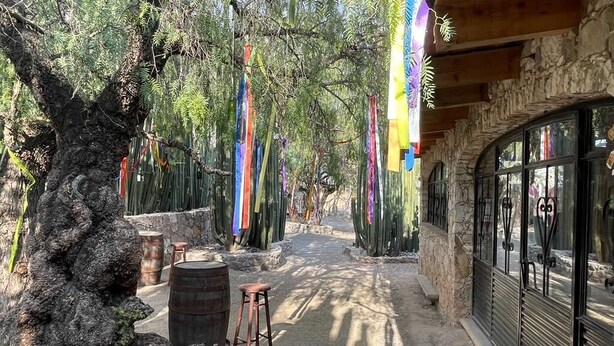 A pathway lined with cacti and colorful ribbons, leading to a building with stone walls and large windows. - La Posada de Don Luis (Ezequiel Montes)