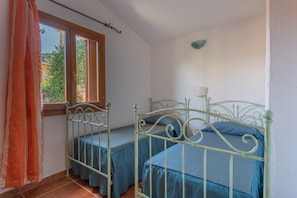 A bedroom with two metal beds, a window, and a wall-mounted lamp.