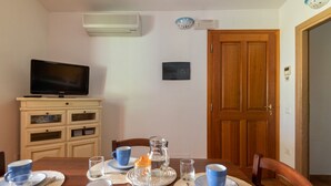 Un coin repas avec une table dressée pour quatre personnes, un téléviseur posé sur un meuble et, au fond, une porte en bois.