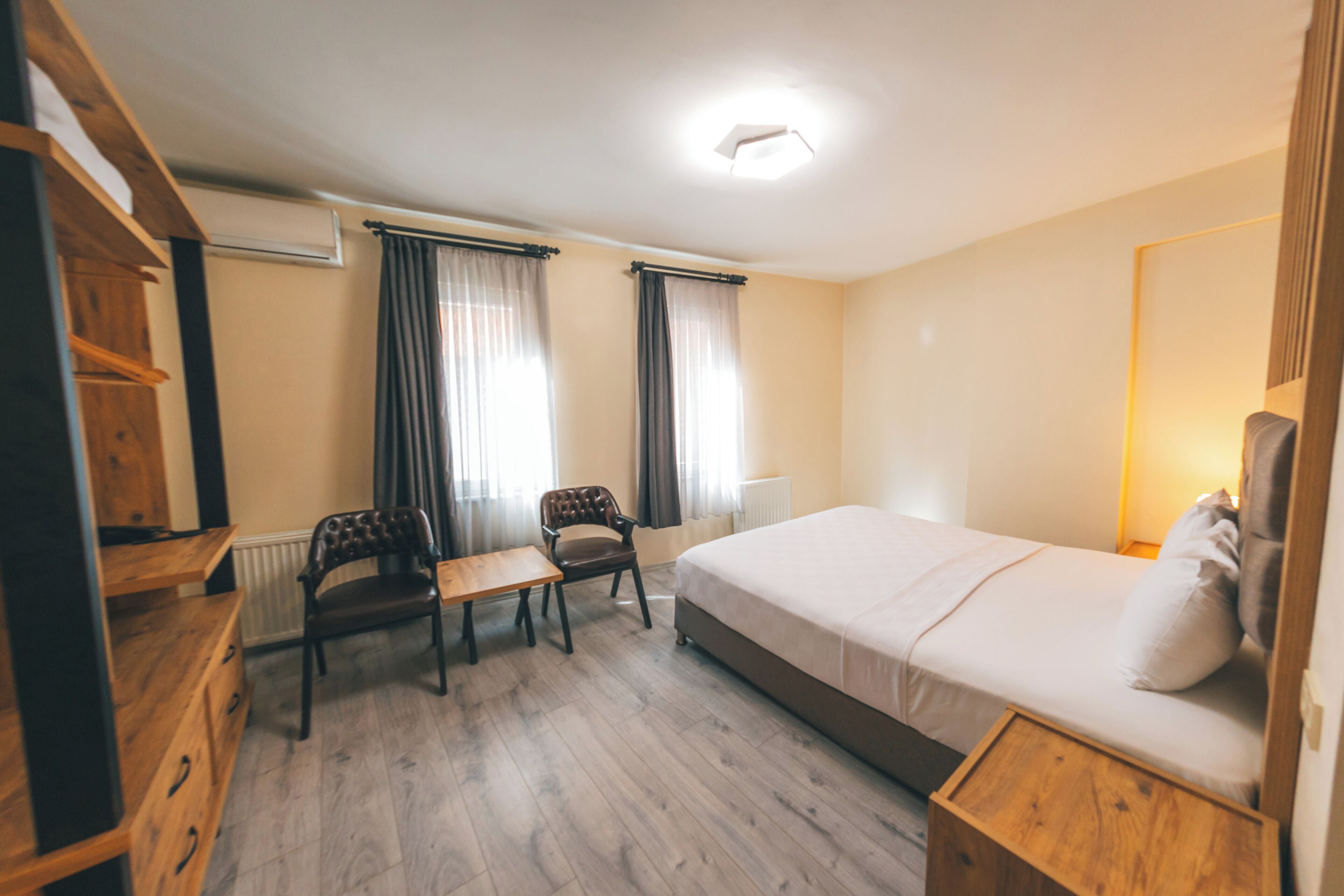 Et hotelværelse med en seng, et skrivebord, to stole, en trækommode og en radiator.