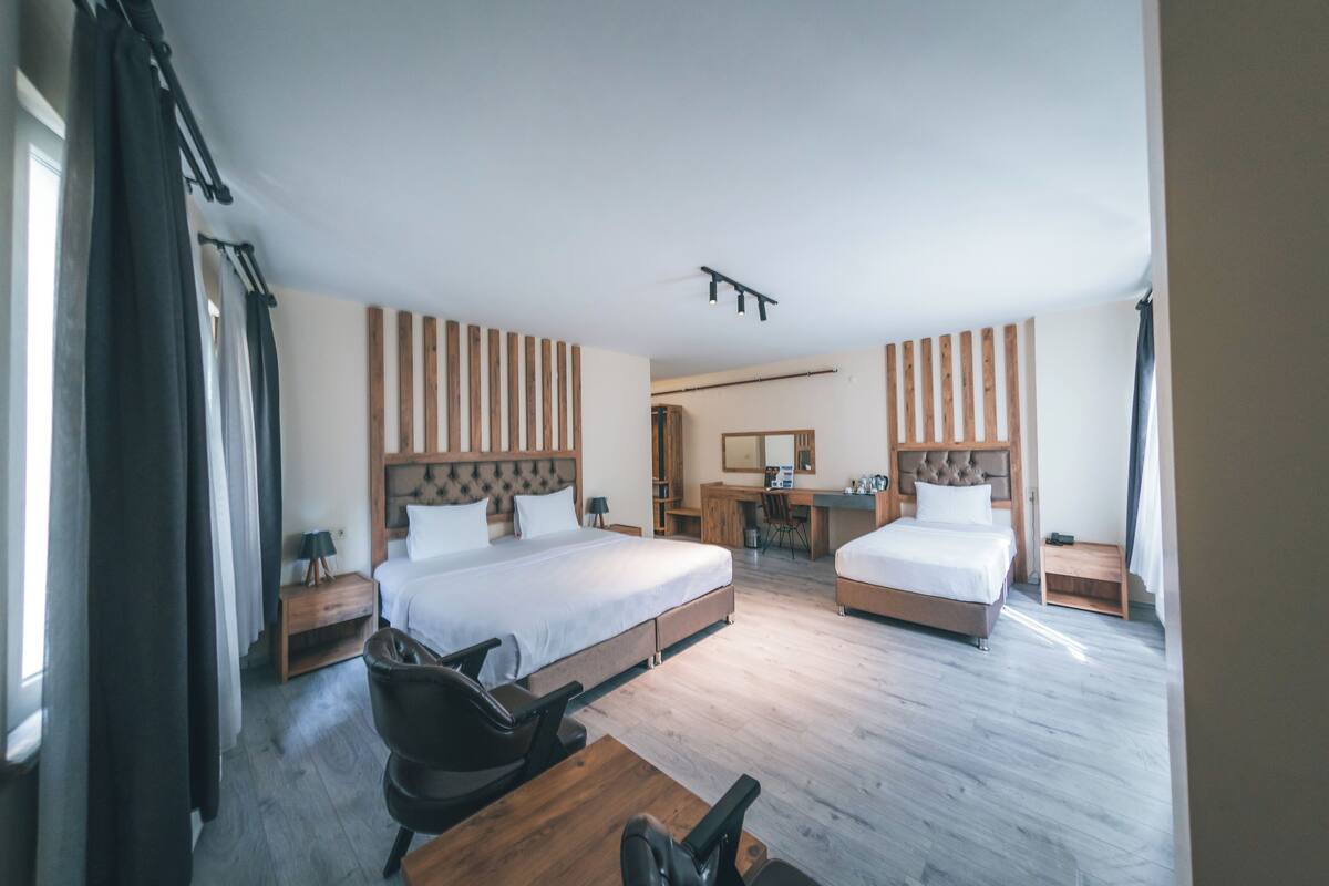 Habitación de hotel con dos camas, un escritorio, una silla, un espejo y suelo de madera.