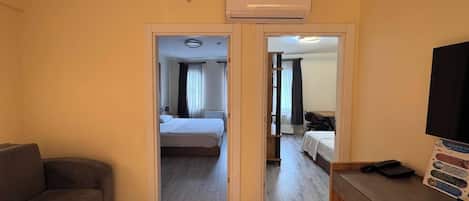 Habitación de hotel con sofá, escritorio y teléfono, y televisor. Cuenta con una cama con cabecera y cortinas, además de otra cama con disposición similar.