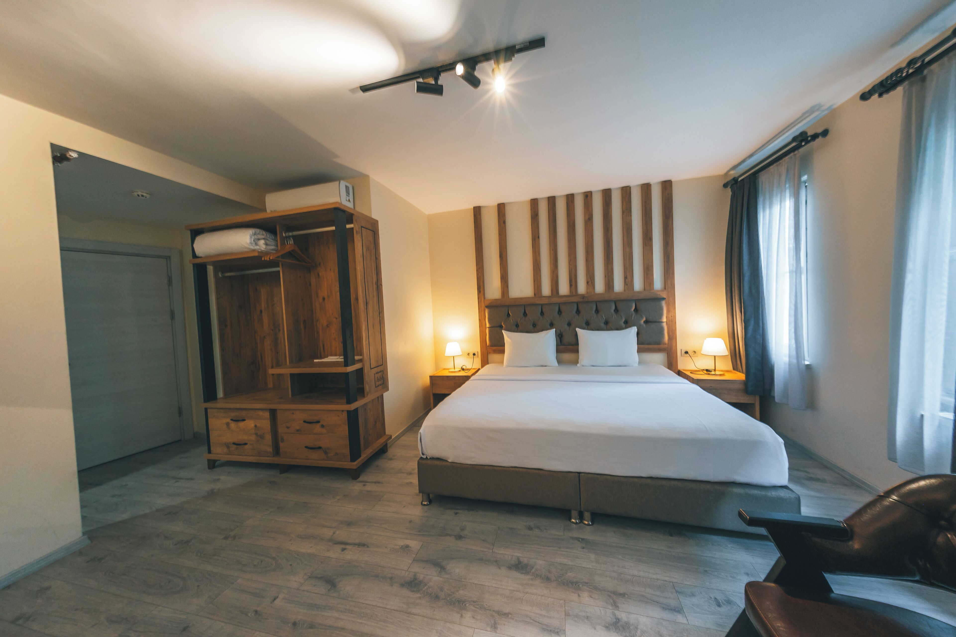 Une chambre d’hôtel avec un grand lit, une armoire en bois, des lampes de chevet et une fenêtre avec des rideaux.