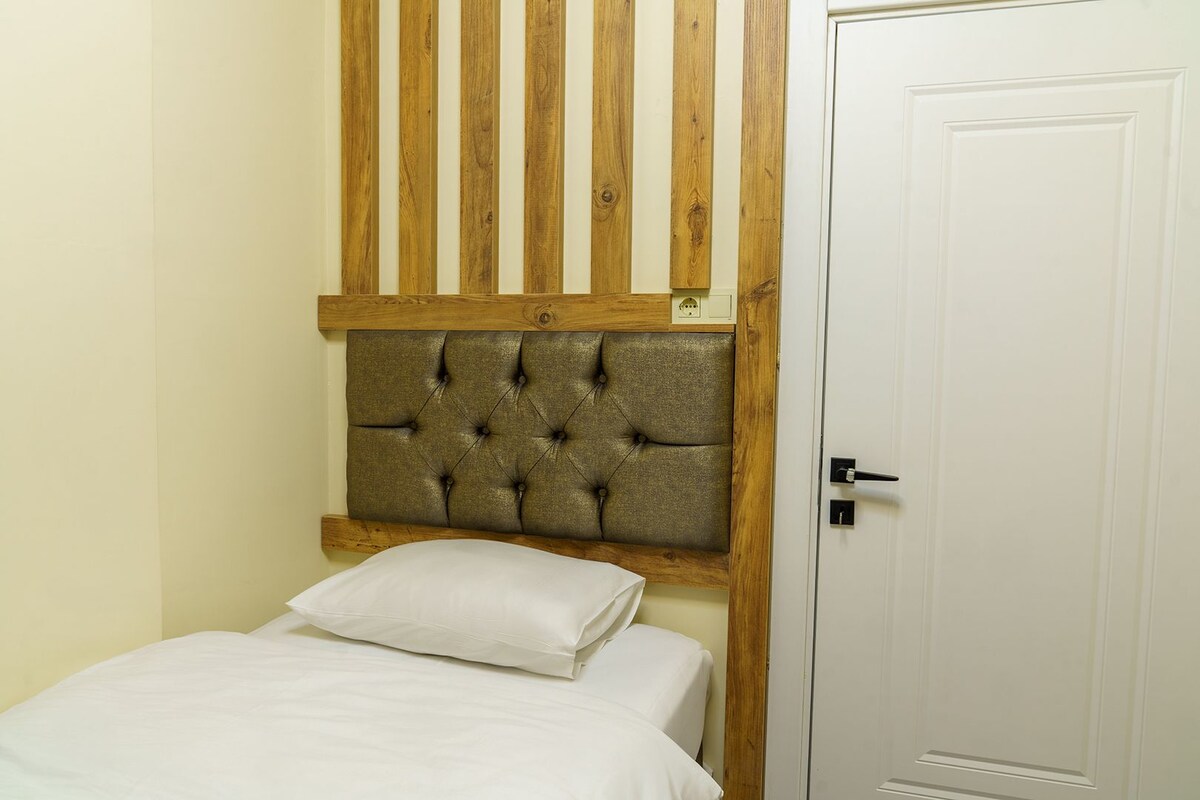 A bedroom with a wooden headboard, a white door, and a bed with white bedding.