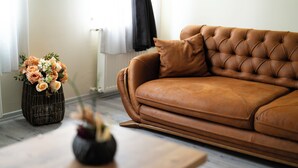 A brown leather sofa with a tufted backrest, a wooden coffee table, and a vase of flowers on the floor. - Grand 464 Otel (Rize)