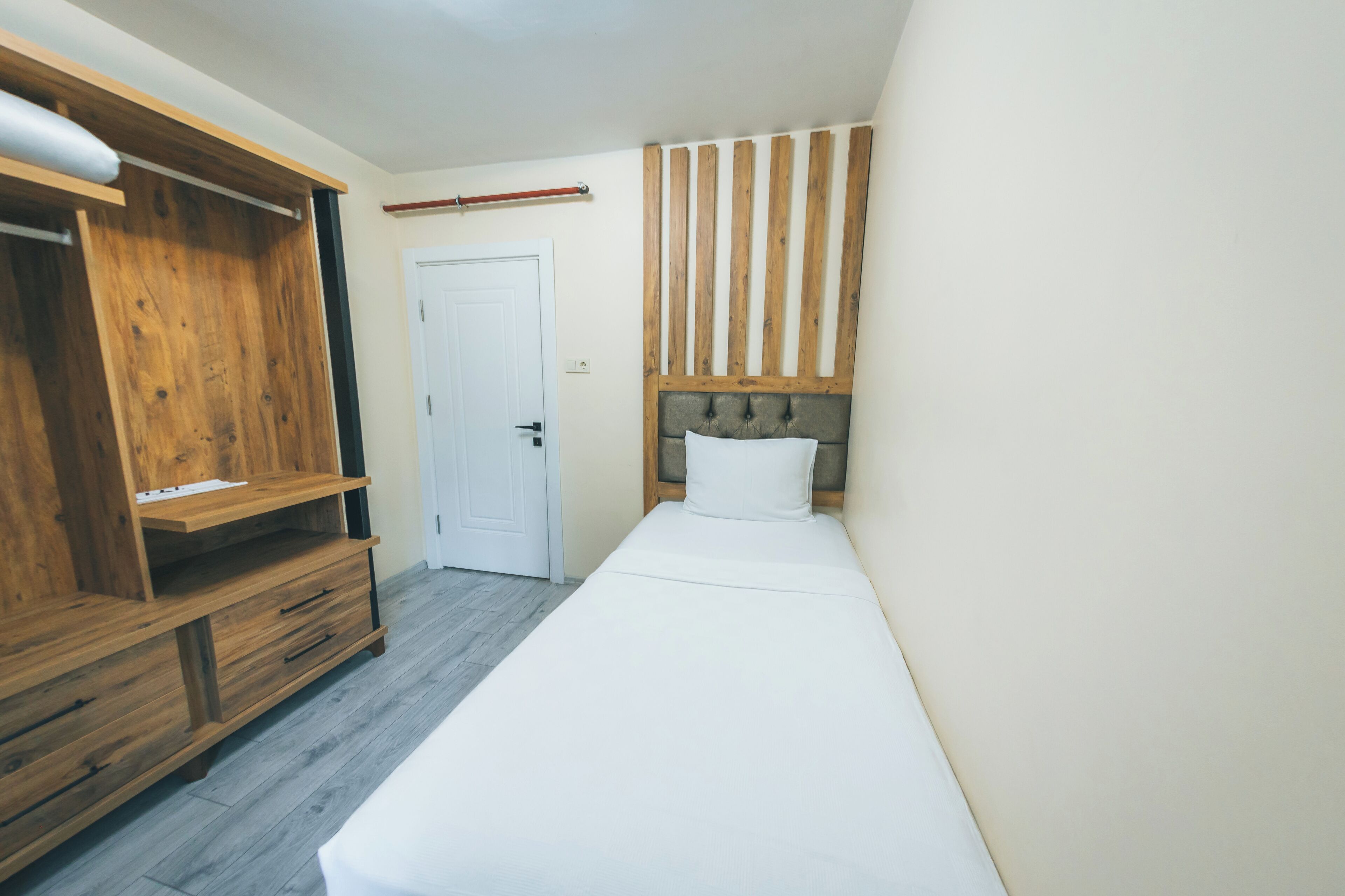 Un dormitorio con un armario de madera, una cama con cabecera y una puerta blanca.