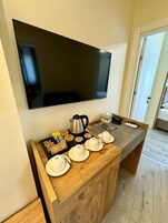 Habitación de hotel con una mesita de noche de madera, un televisor de pantalla plana montado en la pared y una puerta que da a otra habitación.