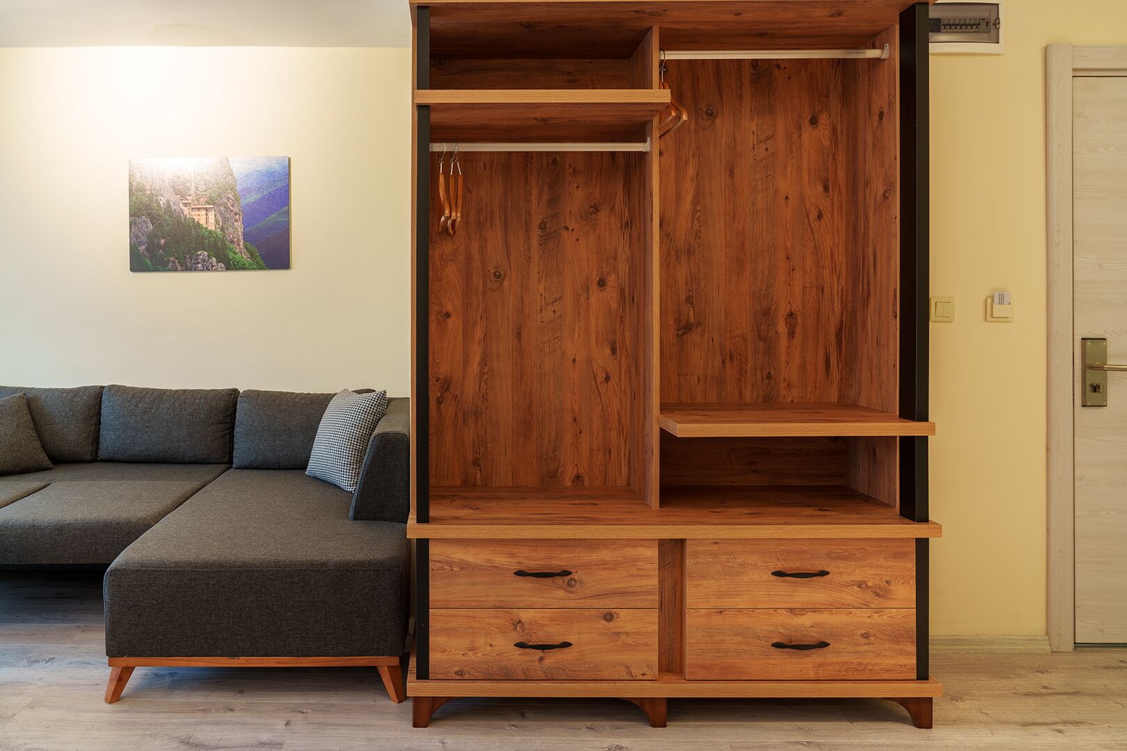 Une armoire en bois dotée de nombreux compartiments et de tiroirs, un canapé gris agrémenté d’un coussin à motifs et une porte avec une poignée.