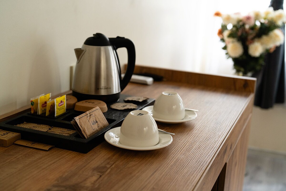 A wooden table with a coffee maker, tea bags, and teacups.
