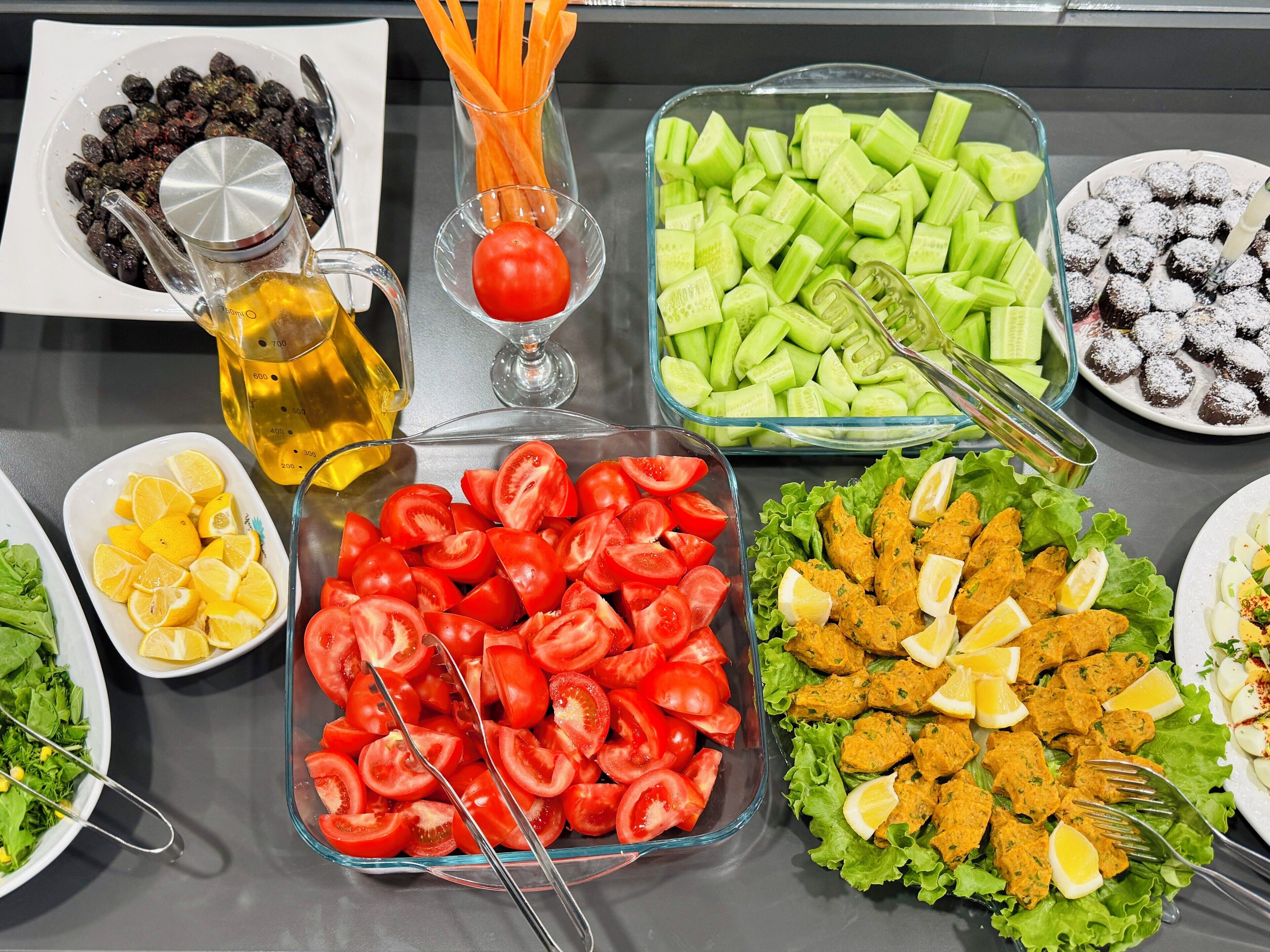 Una mesa de buffet con diversos alimentos, incluyendo tomates en rodajas, pepinos, zanahorias y diferentes ensaladas.