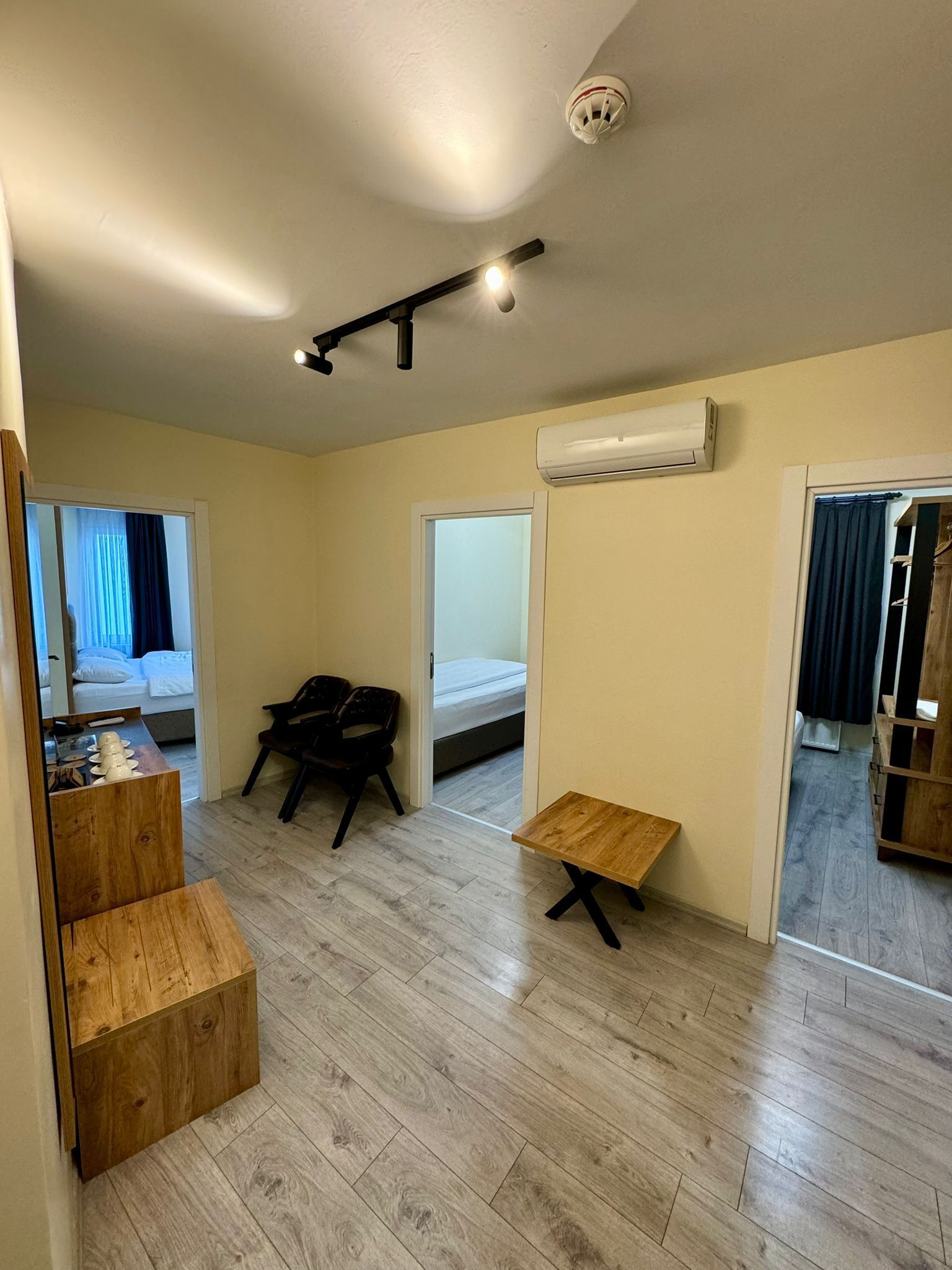A compact room with a bed, a desk, a chair, a small table, and an air conditioning unit.