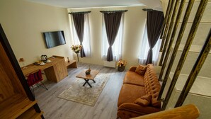 A modern living room with a sofa, a coffee table, a wooden desk, and a TV mounted on the wall. - Grand 464 Otel (Rize)