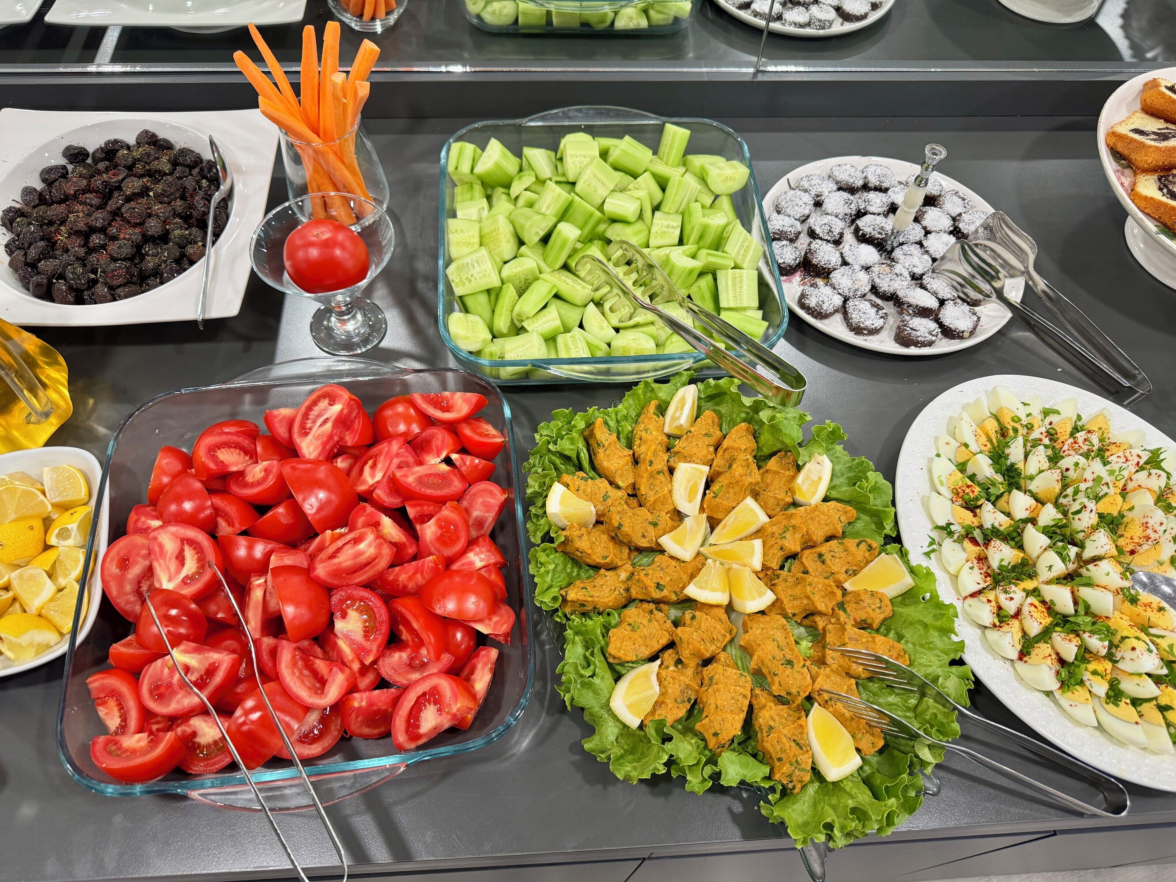 A buffet table with various food items including tomatoes, cucumbers, carrots, and a salad with eggs.