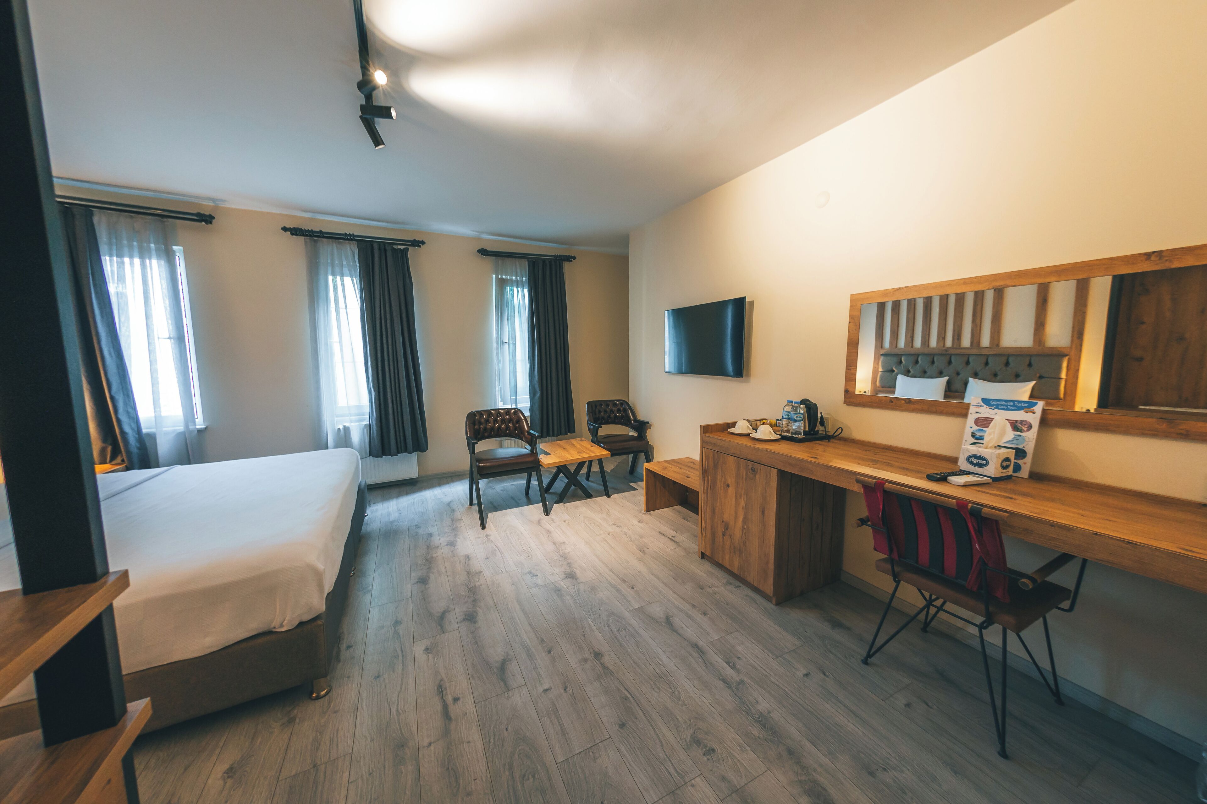 A hotel room with a bed, two chairs, a desk, a flat-screen TV, and a wooden headboard.