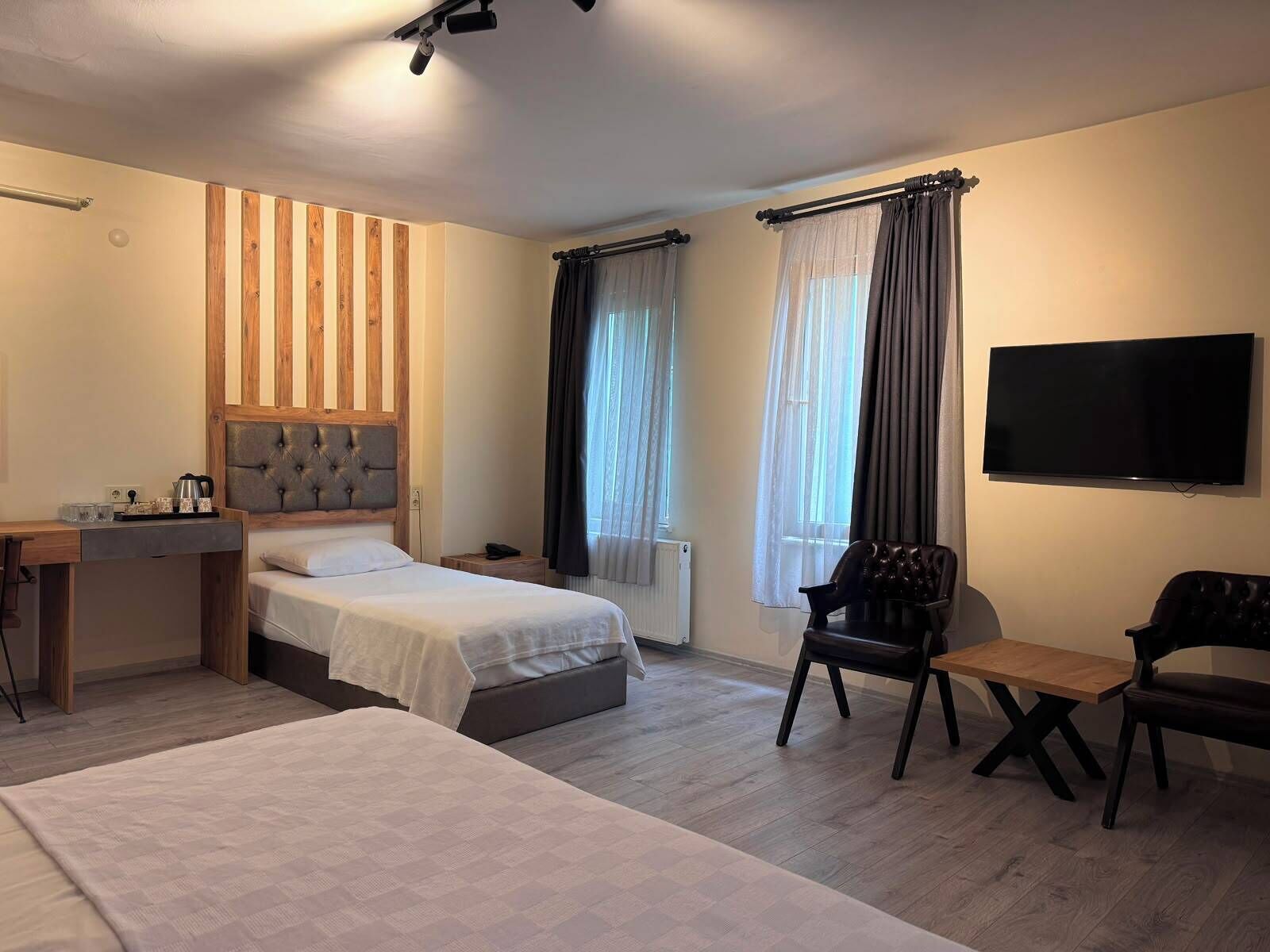 Habitación de hotel con dos camas, un escritorio, una silla, un televisor y un ventanal con cortinas.