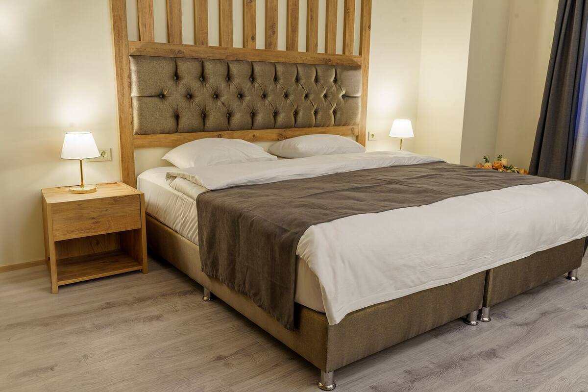 Una cama con cabecera de madera, dos mesitas de noche con lámparas y suelo de madera.