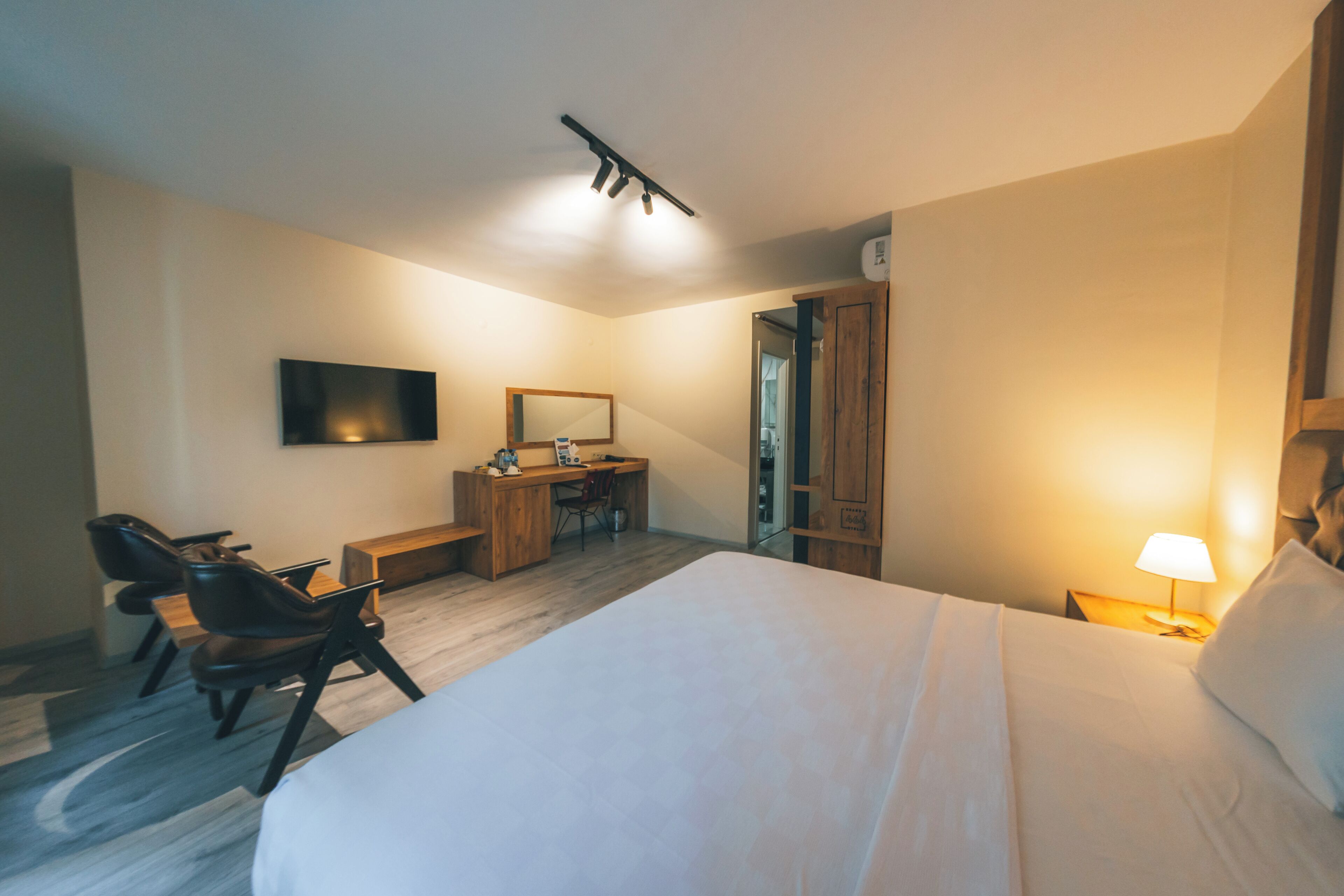 Quarto de hotel com cama, escrivaninha, cadeiras, televisão e espelho.