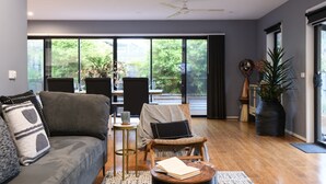 A modern living room with a grey sofa, a wooden coffee table, and a dining area with chairs and a table. - Sutton Lodge (Daylesford)