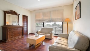 Una sala de estar con un aparador de madera, un sofá color crema, una mesita y una ventana con vista a edificios.