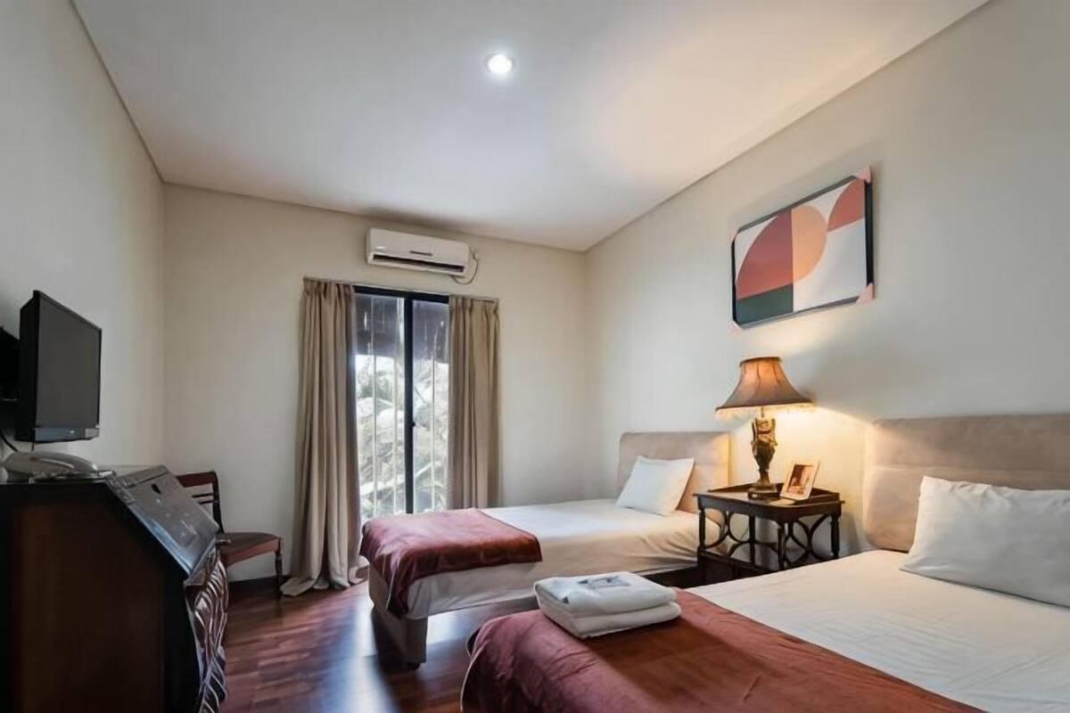 Une chambre d’hôtel avec deux lits, un bureau, une télévision, un appareil de climatisation et une fenêtre avec des rideaux.