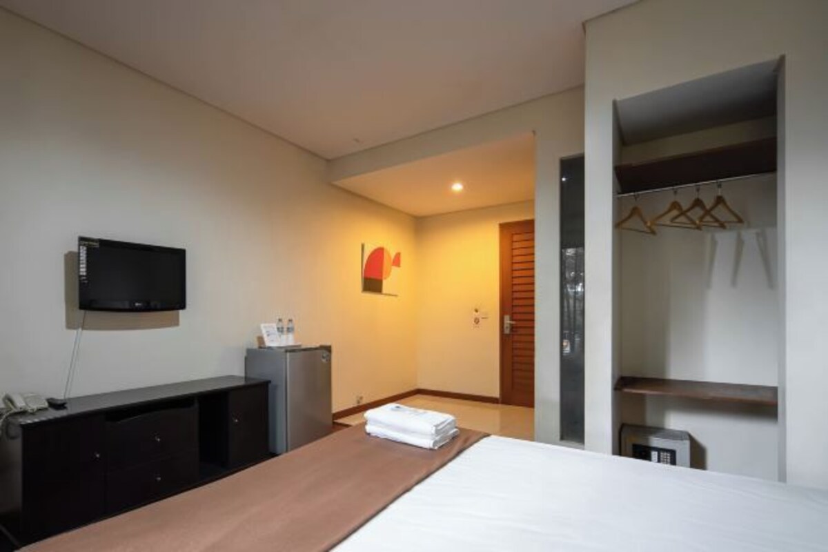 A hotel room with a bed, a desk, a television, a wardrobe, and a door leading to another room.
