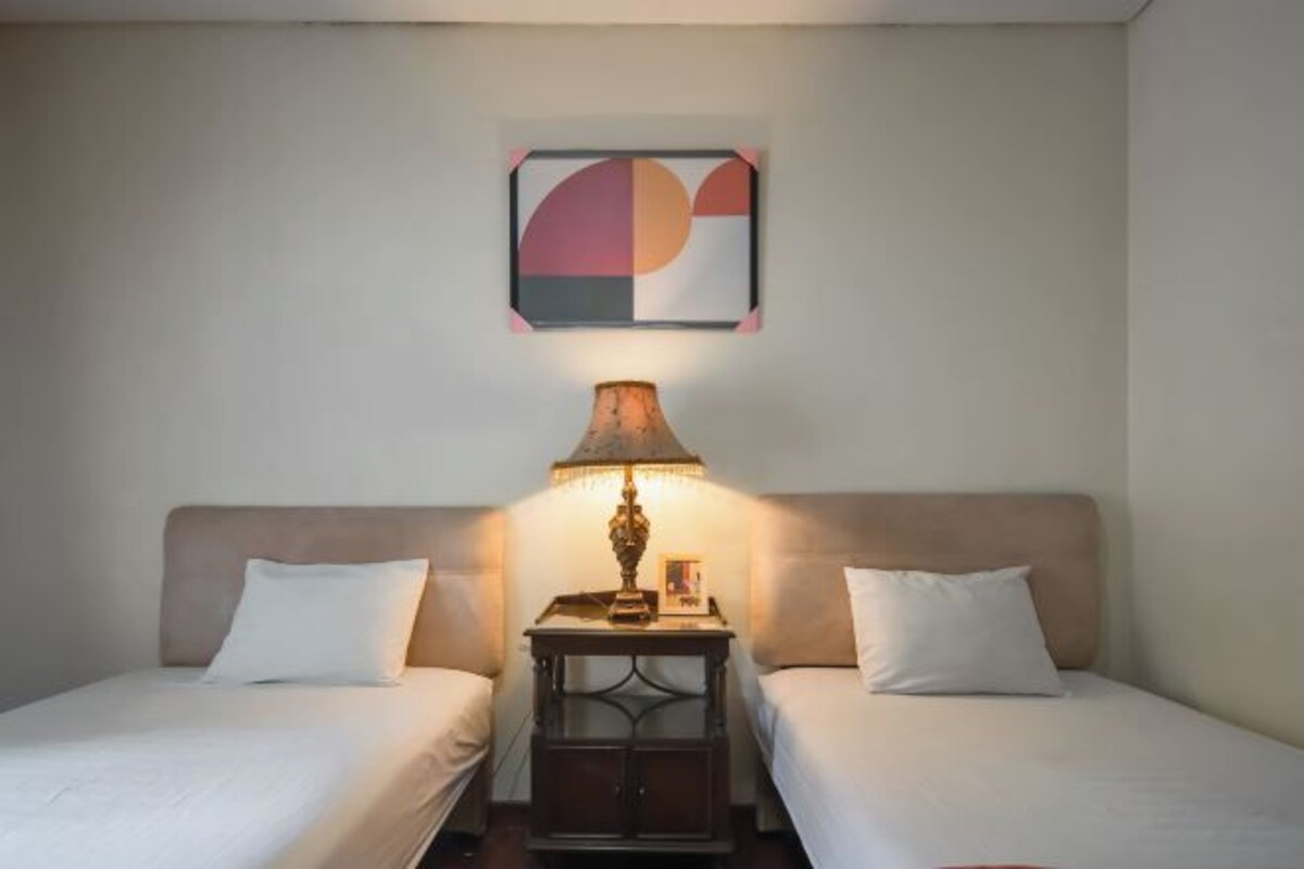 A hotel room with two beds, a nightstand with a lamp, and a wall-mounted abstract artwork.
