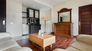 Una habitación de hotel moderna con piso de madera, un sofá, una mesa de centro, un aparador de madera, un espejo y una kitchenette.