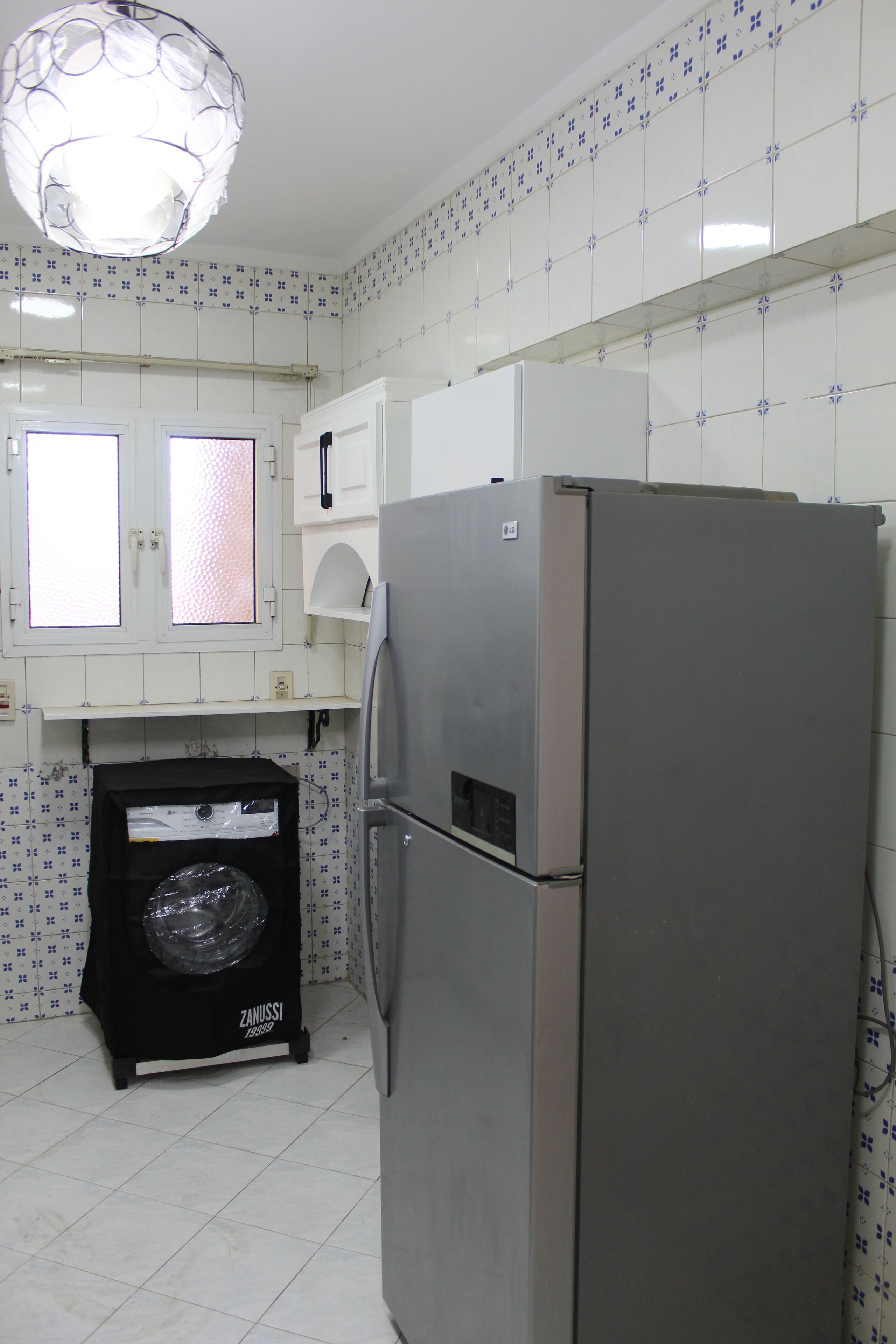 Cuina compacta amb nevera, rentadora i finestra amb vidre mat.