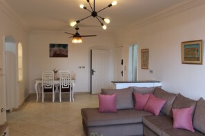 A living room with a brown sofa, white chairs, a dining table, and a ceiling fan.