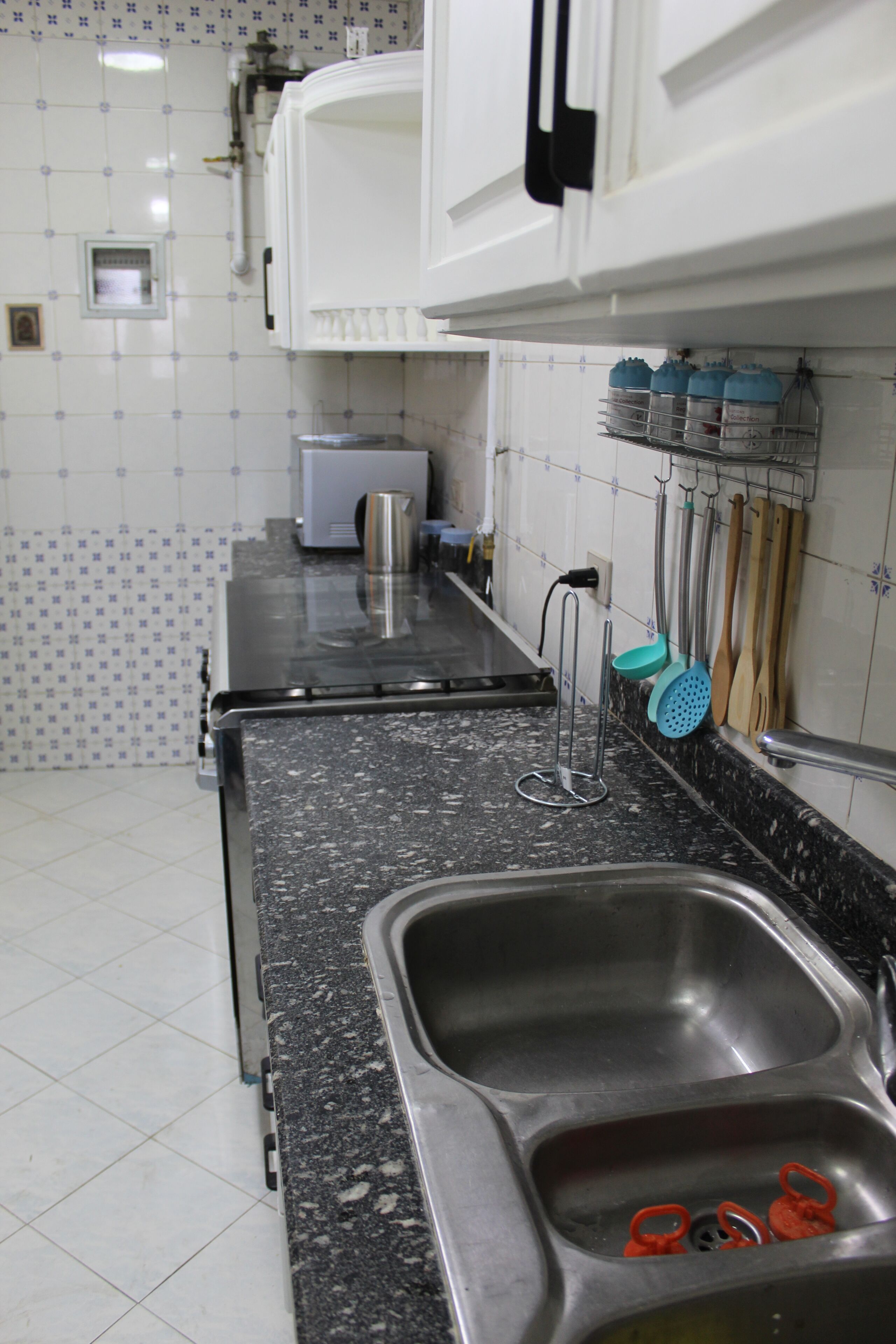 A kitchen with a granite countertop, stainless steel sink, and various utensils hanging on the wall.