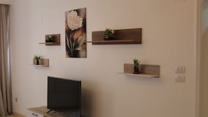 Un soggiorno moderno con una TV a schermo piatto su un mobiletto in legno, circondato da arredamento minimalista tra cui mensole a parete con piante.