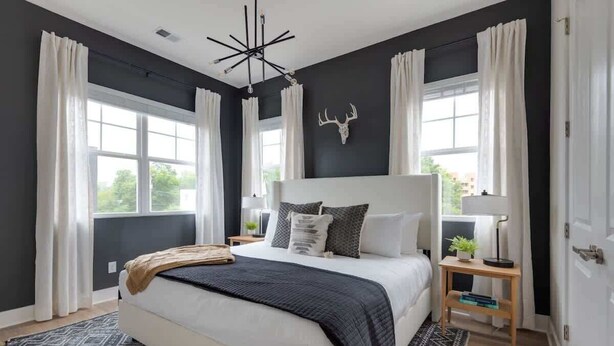 A bedroom with a large bed, two bedside tables, a ceiling light fixture, and a window with curtains. - Wildflower - Rooftop Hot Tub - Game Room (Nashville)