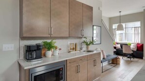 A modern kitchen with stainless steel appliances, wooden cabinets, and a dining area with a sofa and chairs. - Wildflower - Rooftop Hot Tub - Game Room (Nashville)