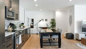 A modern kitchen with dark cabinetry, a built-in microwave, and a large island with seating. - Perch - View Ridge Guest Suite: Cozy 1BR ADU Retreat (Seattle)